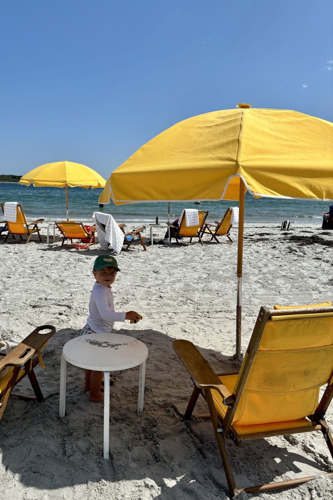 Toddler in a green hat playing in the sand under a yellow umbrella at Goose Rocks Beach