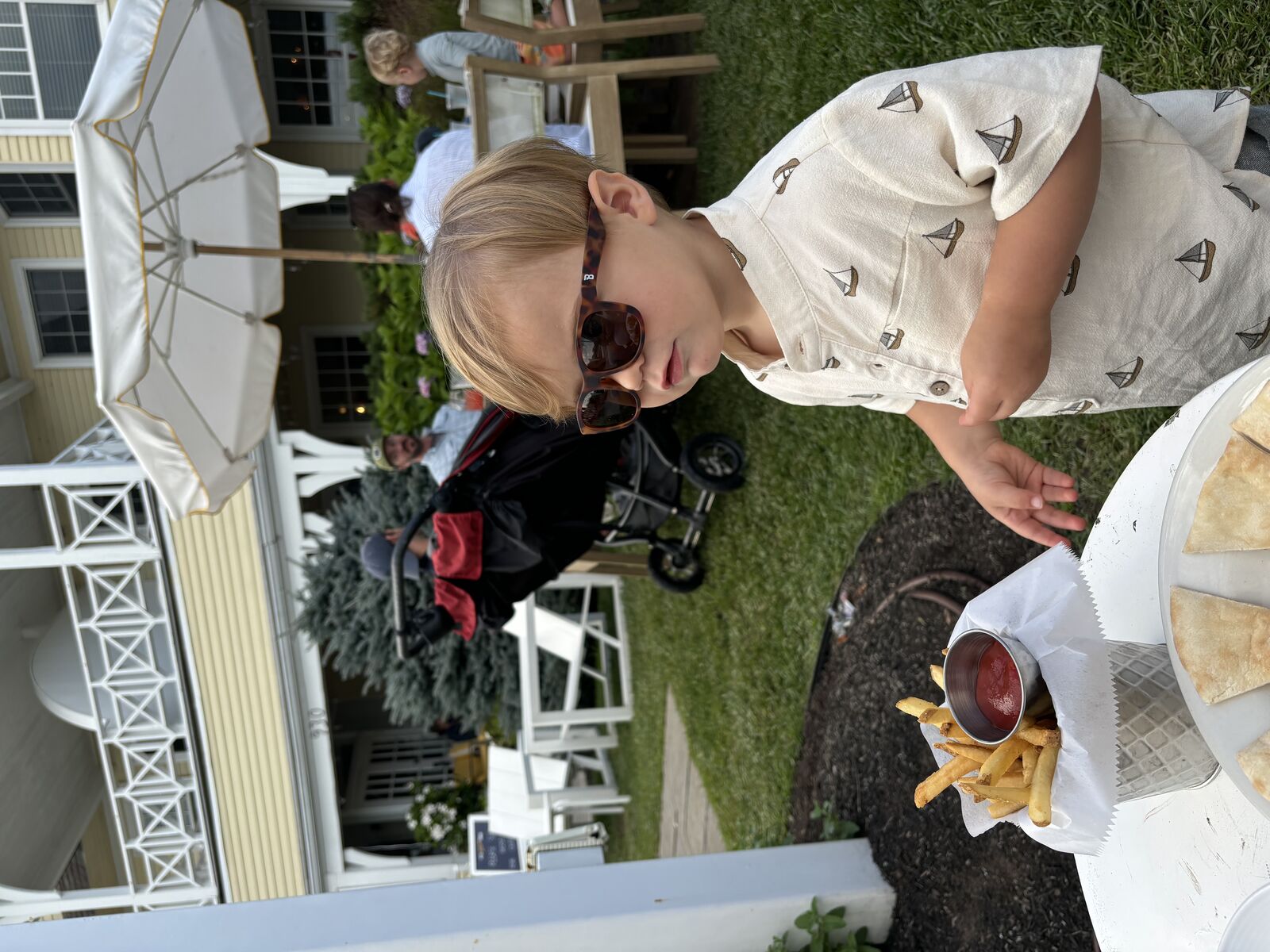 Toddler in sailboat shirt enjoying fries on the lawn at Tides Beach Club's beachside porch
